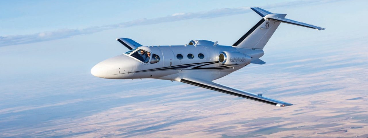 A Cessna Citation Mustang flying over farmlands.
