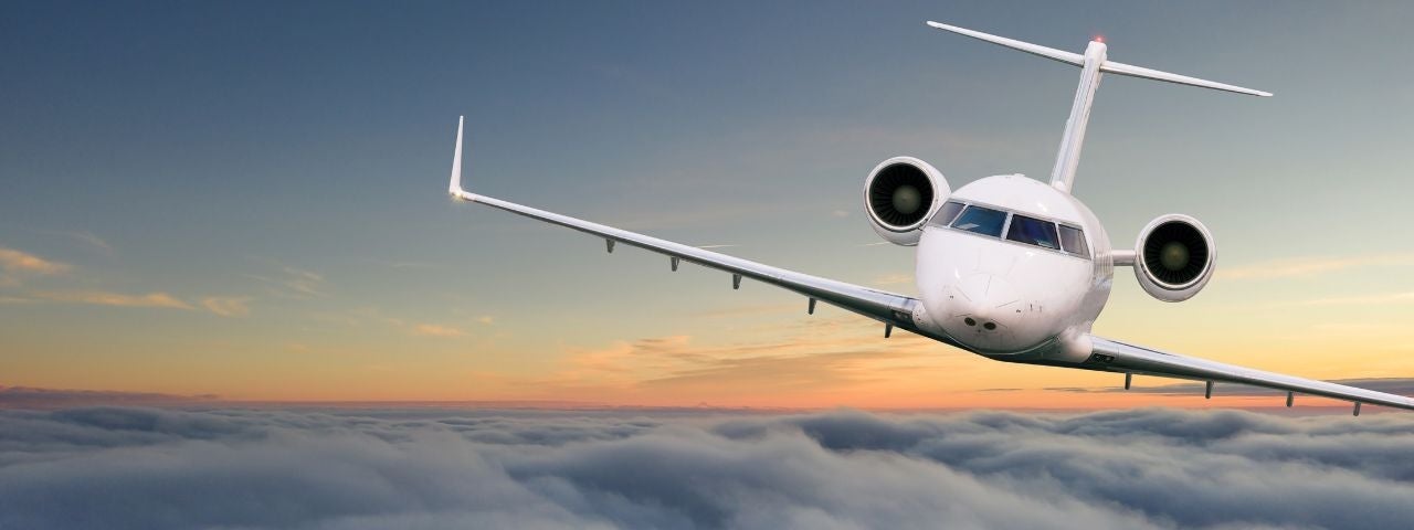 a front view of a private jet flying above the clouds at sunset 