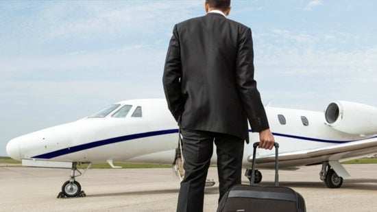 Man walking towards private jet on a runway while dragging a suitcase
