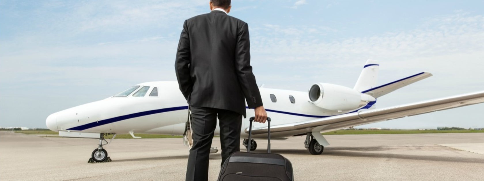 Man walking towards private jet on a runway while dragging a suitcase