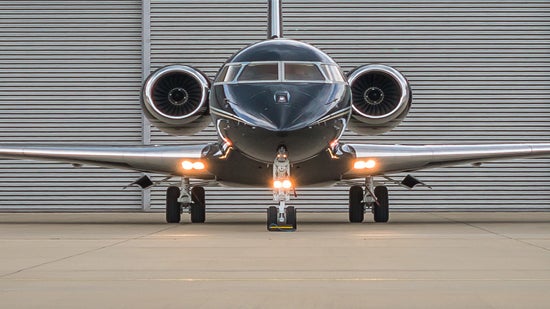 Front view of a black and silver private jet in front of an airport hangar