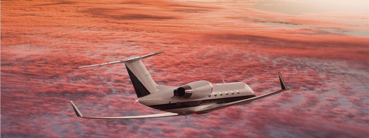 Private business jet flying in red sky