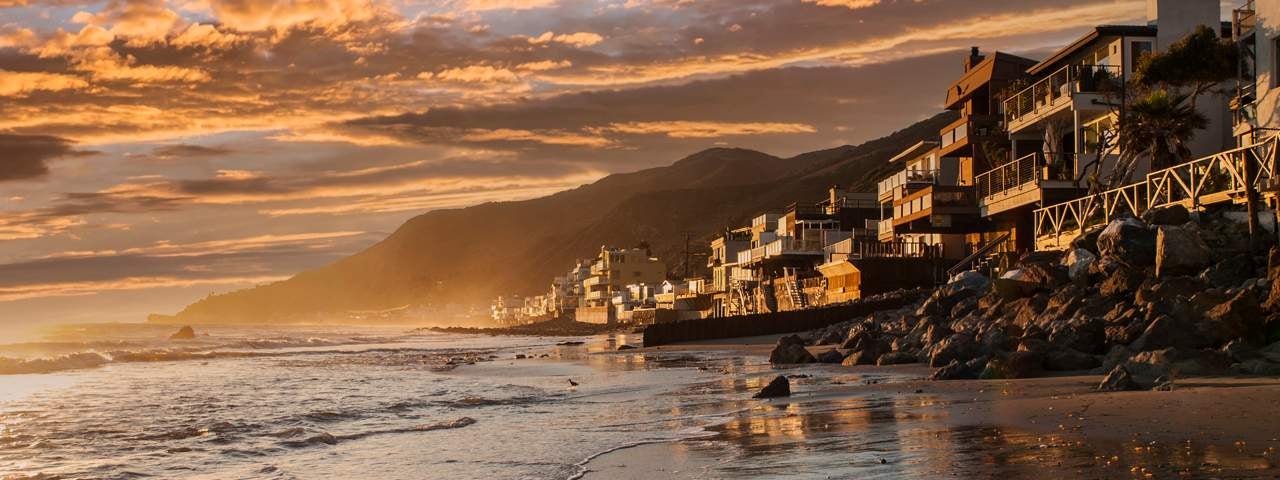 Houses on a beach in Malibu with the sunset light and the sea in the foreground